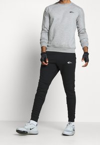 Felpa grigia con dettagli a coste sulle spalle, abbinata a pantaloni jogger neri con inserti sulle ginocchia. Guanti neri e sneakers grigio chiaro completano il look.