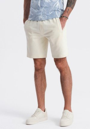 Cremefarvede shorts lavet af bomuld, med en afslappet pasform, sidelommer og stikninger. Båret med lysfarvede sneakers.
