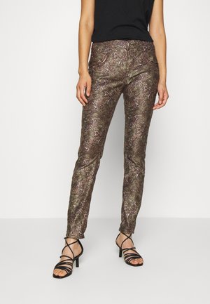 Slim fit bukser med indviklet brunt og gyldent paisleymønster, båret med sorte sandaler med hæl og stropper og en sort top.