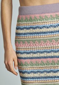 Gebreide rok met horizontale strepen in pastelkleuren: roze, groen, blauw en crème, met kantpatronen en een geribde lila tailleband.