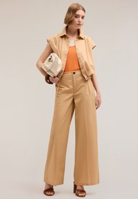 Beige cropped shirt over orange top, paired with wide beige trousers. Accessories include a white bag and brown heeled sandals.