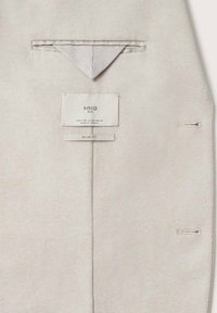 Beżowa, fakturowana tkanina z trójkątną, złożoną chusteczką w kieszeni oraz dwoma metkami z napisem "MNG MAN", rozmiar 40, slim fit, wyprodukowano w Wietnamie.