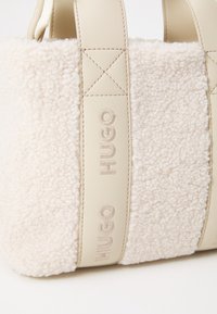 Creme faux shearling taske med struktureret overflade, accentueret af beige læderstropper med prægede "HUGO"-brand og syede detaljer.