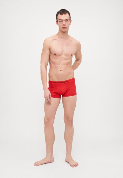 Boxer aderenti in cotone rosso con elastico in vita, caratterizzati dal logo "Emporio Armani" in nero. Texture liscia, design aderente.