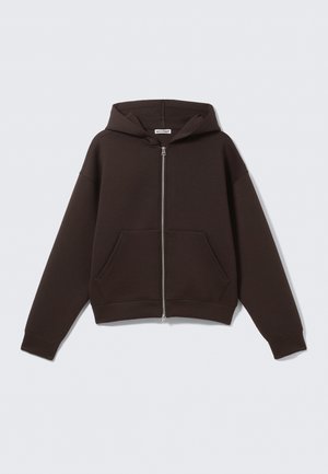 Tumepruun zipiga kapuutsiga pusa, millel on esitaskud ja kapuuts, esitatud valgel taustal.