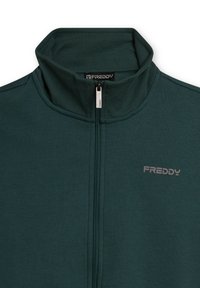 Chaqueta de cremallera verde oscuro con cuello alto, textura suave, logo de Freddy en gris en el pecho izquierdo, mostrando un diseño minimalista.