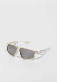 Rektangulære solbriller med guldtonede metalrammer, mørkt tonede linser og gennemsigtige stænger med Oakley-logo på hvid baggrund.