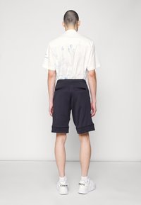 Biała koszula z krótkim rękawem z niebieskim wzorem graficznym na plecach, w zestawieniu z czarnymi szortami z elastycznym pasem i bocznymi kieszeniami. Białe trampki.