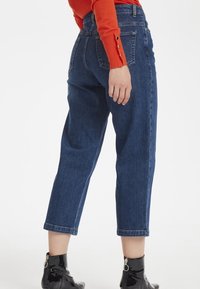 Pantalones vaqueros de mezclilla azul oscuro con un ajuste recto, recortados en el tobillo, con bolsillos traseros y combinados con botines negros de charol.
