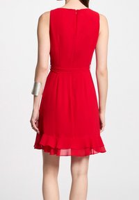 Robe rouge avec un corsage ajusté, une jupe évasée et un ourlet à volants. Présente un dos en forme de goutte d'eau et une fine ceinture nouée à la taille. Texture lisse.