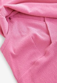 Roze textiel met een subtiele ribbelstructuur, met plooien en kreukels die de lichte en zachte kwaliteit van het materiaal benadrukken.