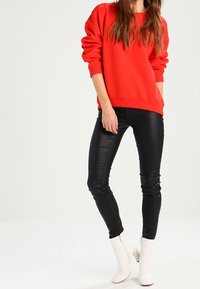 Felpa rossa oversize, pantaloni neri in faux leather aderenti e stivaletti bianchi alla caviglia. Design semplice, texture morbida e contrasto di colori audace.