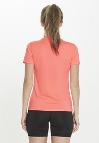 Short-sleeve, fitted T-shirt in bright coral, made of smooth synthetic material, featuring a classic crew neck and minimal seams.