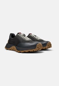 Black athletic shoes with a textured mesh upper, white laces, and a thick gum rubber sole featuring a rugged tread pattern.