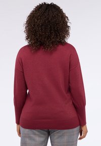 Bordeaux glitzernder Pullover mit lockerer Passform, überschnittenen Schultern und geripptem Saum. Ausgestattet mit langen Ärmeln und einer weichen Textur.