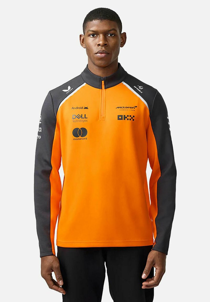 Kurtka wyścigowa McLaren z pomarańczowymi i szarymi blokami kolorystycznymi, zapinana na ćwierć zamka, z logo oraz sportową, dopasowaną sylwetką.