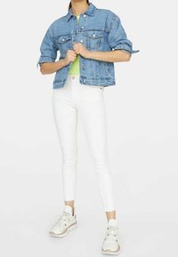 Chaqueta de mezclilla en azul claro, con dos bolsillos frontales y mangas remangadas. Combinada con unos pantalones skinny blancos y zapatillas blancas.