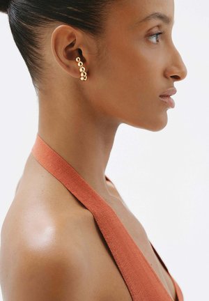 Pendiente multicolor en tono dorado con un diseño sin costuras, llevado en la oreja izquierda, destacando una textura suave contra la piel.