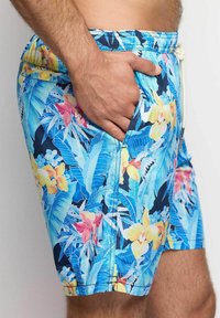 Bañadores para hombres en un azul vibrante con un patrón floral tropical que presenta flores amarillas y rosas, bolsillos laterales y cinturilla elástica.