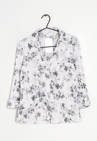 Chemise à manches longues avec un col en V, en tissu blanc présentant un motif floral gris et des rayures subtiles, détail de boutons sur les poignets retroussés.