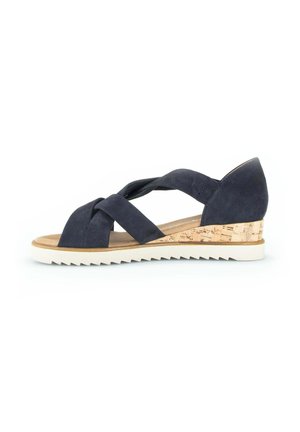 Sandale en daim bleu marine avec des brides croisées, talon compensé en liège, semelle intérieure rembourrée et semelle blanche rainurée sur fond neutre.