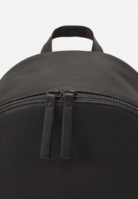 Zaino nero realizzato in tessuto testurizzato, con un top arrotondato, chiusura a doppia zip con maniglie in pelle nera e una maniglia superiore per il trasporto.