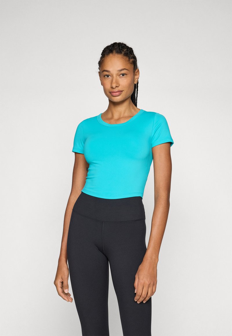 Teal kortärmad crop top med rund halsringning, tillsammans med svarta högmidjade leggings; len yta och figurnära design.