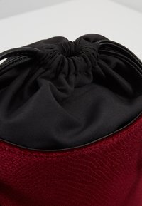 Rode stoffen tas met een zwarte trekkoordsluiting, voorzien van een gladde zwarte voering en een samengevouwen bovenkant voor gemakkelijke toegang.