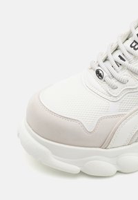 Baskets blanches de sport avec une tige en maille texturée, des accents en suède et une semelle blanche épaisse avec des sections arrondies distinctes.
