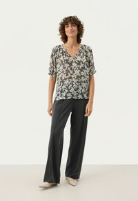 Bluse med blomstermønster i gennemsigtigt stof med V-hals og korte ærmer. Kombinationen er med mørke, vide bukser og beige sko.