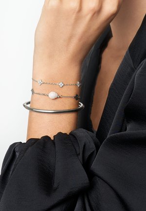 Silver bracelet set featuring a slim bangle and layered chains with star-shaped accents and a seashell detail. Worn on a wrist.
