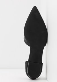 Chaussure noire à bout pointu avec un motif texturé en crocodile et un talon plat, présentée sur un fond blanc. Détails de la semelle et du talon visibles.