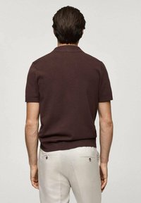 Brązowa, ciemna koszulka polo z krótkim rękawem i płaskim kołnierzykiem. Gładka faktura i dopasowany krój, zestawiona z jasnymi spodniami.
