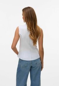 Witte mouwloze top met een gestructureerd oppervlak, aansluitende silhouet en gebogen zoom. Gecombineerd met losse blauwe denim jeans.