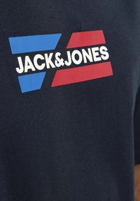 Mørkeblå bomulds t-shirt med hvid tekst "JACK & JONES" med blå og røde geometriske former ovenfor. Glat struktur, korte ærmer.