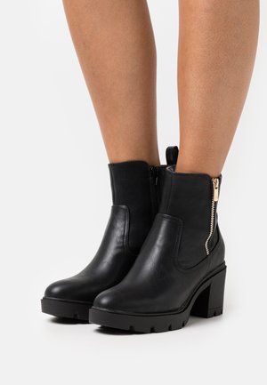 Stivaletti neri in pelle liscia, con tacco spesso, cerniera laterale con dettagli dorati e suola in gomma texturizzata.