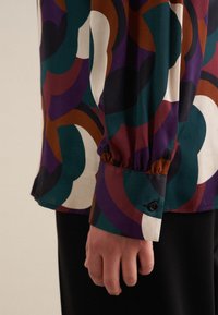Camicia a maniche lunghe con un vivace motivo geometrico multicolore, dotata di un bottone nero al polsino, con una texture setosa e una vestibilità morbida.
