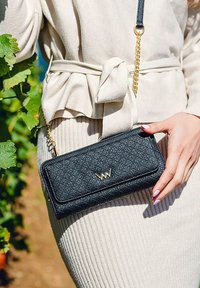 Black quilted crossbody bag with gold hardware, featuring a textured surface, rectangular shape, and a detachable chain strap.
