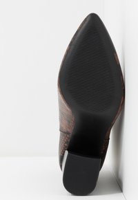 Semelle de chaussure à talon haut imprimée serpent marron avec un design à bout pointu. Grip en caoutchouc noir texturé sur le dessous et talon solide et structuré.
