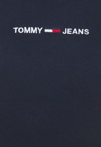 T-shirt en coton marine avec un texte brodé blanc "TOMMY" et "JEANS" et un accent de logo rouge et blanc au centre.