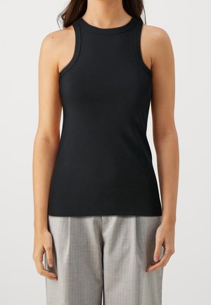 Czarny bezrękawnik z gładkiej tkaniny, z wysokim kołnierzem i dopasowanym krojem. Połączony z jasnoszarymi spodniami w cienkie paski.