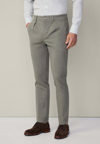 Grau maßgeschneiderte Hose aus Baumwollmix, mit flacher Front, Seitentaschen und slim fit Design. Kombiniert mit braunen Wildlederschnürschuhen.