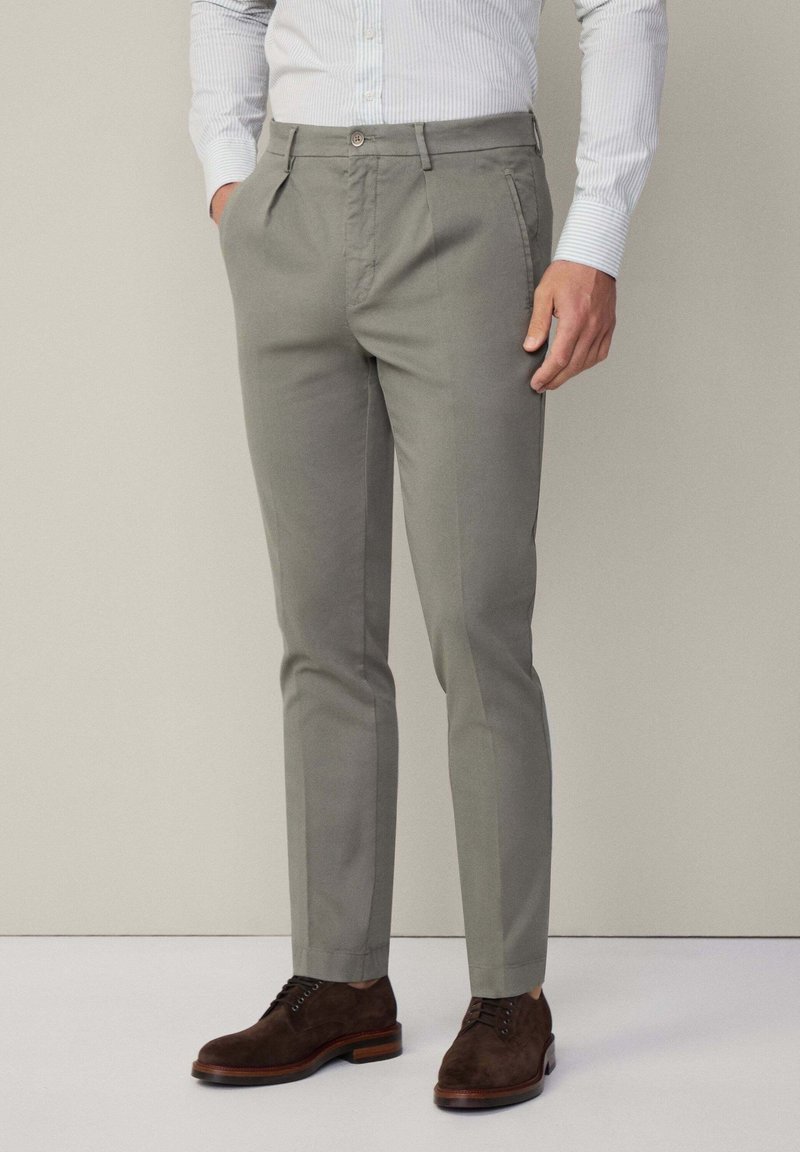 Grau maßgeschneiderte Hose aus Baumwollmix, mit flacher Front, Seitentaschen und slim fit Design. Kombiniert mit braunen Wildlederschnürschuhen.
