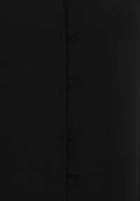 Indumento in tessuto nero con chiusura frontale a bottoni rotondi, texture liscia e silhouette dritta.