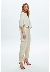 Korte, lichtbeige top met losse mouwen, gecombineerd met lichtbeige cargobroek met zijzakken en gathered enkels. Strappy hakken maken de look compleet.