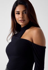 Zwarte top met lange mouwen met een asymmetrische halslijn en een uitsnijding bij één schouder. Soepele, rekbare stof met een nauwsluitend ontwerp.