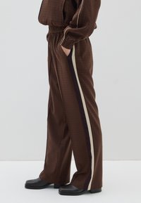 Bruine geruite losvallende broek met een contrasterende beige en donkere stripe langs de zijkant. Beschikt over een elastische tailleband en zakken.