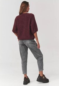 Burgundowy, puszysty sweter z krótkimi rękawami, zestawiony z szarymi, zwężanymi dżinsami i masywnymi czarnymi sneakersami. Wyświetlony widok z tyłu.