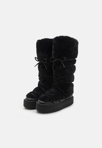 Svarta, pälsfodrade stövlar med en hög, rynkad skaft, utrustade med svarta snörningar och en tjock svart sula. Materialet verkar mjukt och plyschigt.