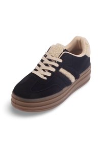 Sneaker en suède noir avec une semelle en caoutchouc, un col en fausse fourrure crème et des lacets crème. Présente des rayures latérales texturées et un design de bout arrondi.